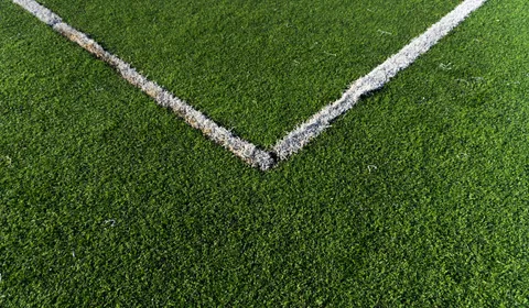 Worn artificial turf sports field under harsh direct sun